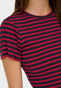 Ribbet t-shirt i marineblå med pink vandrette striber, med en rund halsudskæring og korte ærmer. Blød tekstur med et tætsiddende design.