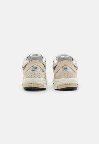 Chaussures de sport beige et grises en mesh et daim, dotées d'un col rembourré, d'accents texturés et d'une semelle extérieure en caoutchouc.