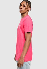 T-shirt di cotone rosa con maniche corte, presenta una stampa bianca con il testo "MAI IN TEMPO" sul davanti, design con scollatura a girocollo standard.