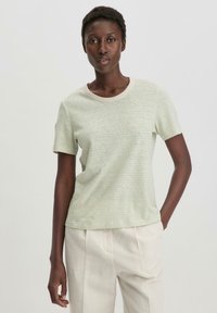 Lichtgroene, kortegedragen t-shirt met subtiele strepen, ronde halslijn en zachte textuur, gecombineerd met crèmekleurige broek.