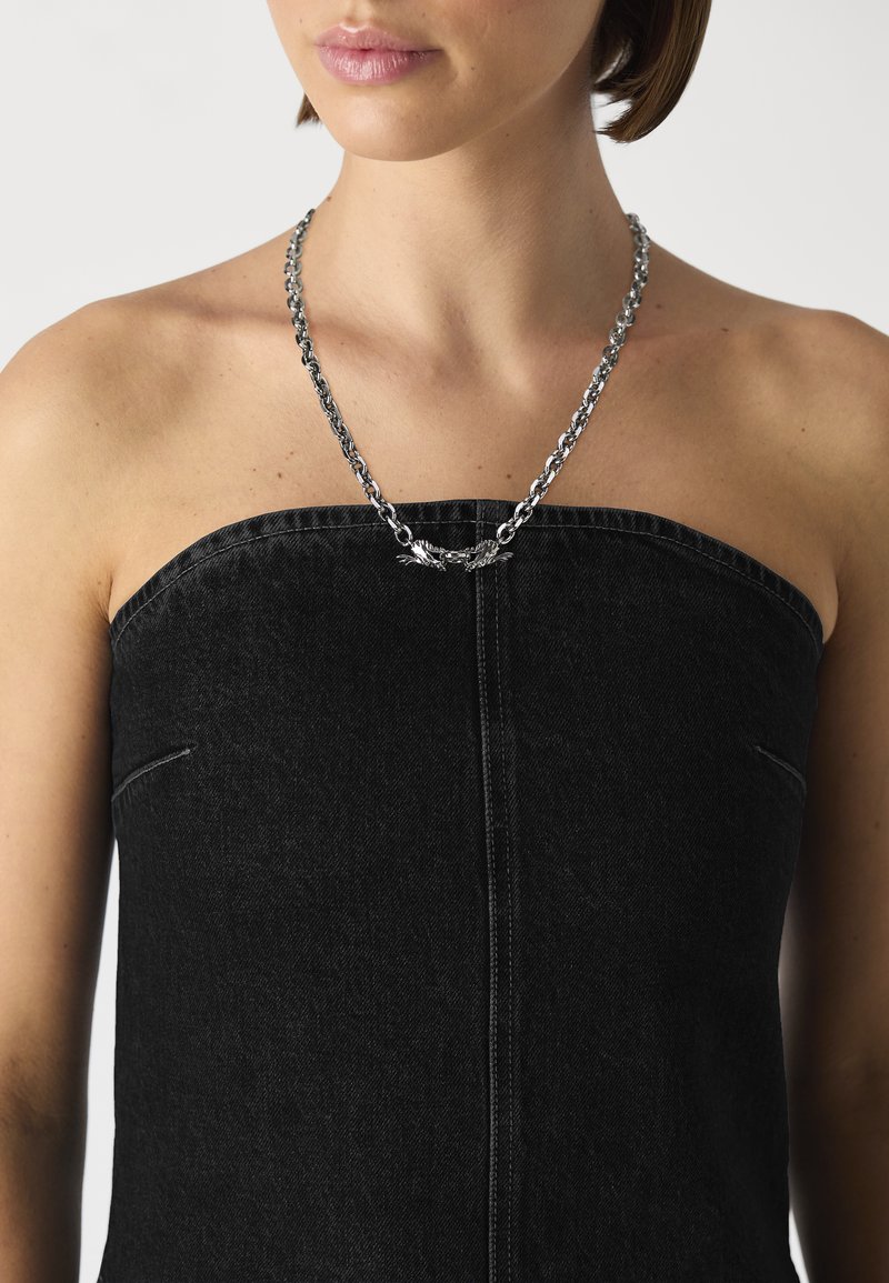 Silver chain necklace with a textured finish and ornate central detail, worn with a strapless black denim top featuring a straight neckline.