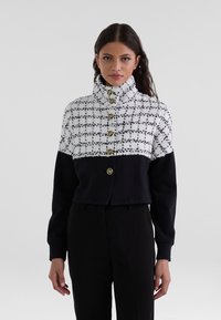 Cropped jacket with a white and black checked upper, featuring gold buttons; black sleeves and lower panel; textured fabric, high collar.