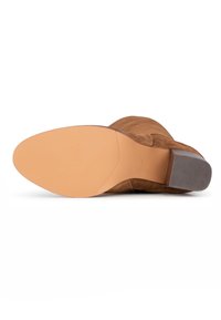 Bottine en daim marron avec une semelle lisse, un talon texturé et un bout pointu. La semelle présente des motifs de grip pour une meilleure adhérence.