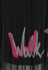 Schwarzer, plissierter Stoff mit großen rosa und grauen Pinselstrichtexten, die teilweise im mittleren Bereich sichtbar sind.