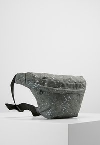 Riñonera de tela verde oscura con un patrón floral en tonos más claros. Cuenta con una correa ajustable negra y cierre de cremallera suave.