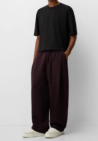 Camiseta negra corta combinada con pantalones holgados de burdeos oscuro, con bolsillos laterales y zapatillas blancas con detalles texturizados.