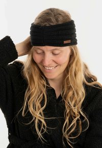 Fascia nera in maglia con un design strutturato, dotata di un piccolo etichetta marrone. Il modello indossa una veste scura e testurizzata e ha lunghi capelli mossi.