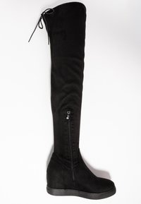 Botte noire montant jusqu'à la cuisse, fabriquée en matériau doux avec une texture lisse. Dotée d'une fermeture éclair latérale et d'un talon compensé, affichant un design élégant.