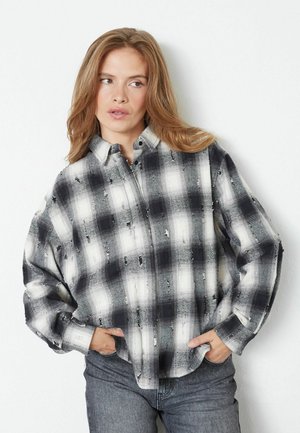 Long-sleeve plaid shirt in black and white with a loose fit, featuring a buttoned collar and distressed accents on the fabric.