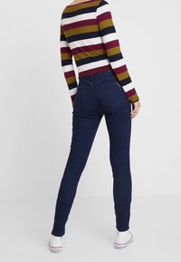 Jeans oscuros ajustados con una textura suave, combinados con una camiseta de manga larga a rayas multicolor. Bolsillos traseros notables y un branding sutil.