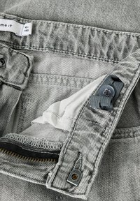 Hallide teksased, millel on lukuga ja metallist nupuklause. Sisevoodril on valge vooder mustade õmblustega ning hall reguleeritav rihm.