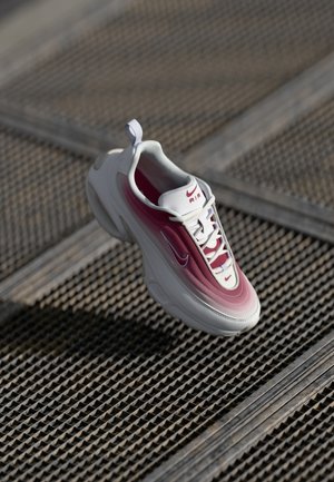 Biało-różony but do biegania Nike Air ze sznurowadłami na teksturowanej metalowej powierzchni w naturalnym świetle.