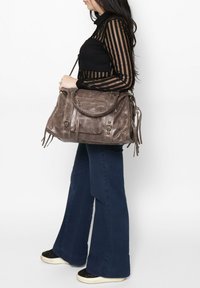 Grijze suède handtas met meerdere zakken, metalen hardware accenten en franjerand. Voorzien van een brede schouderriem voor gemakkelijk dragen.