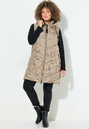 Chaleco acolchado beige con patrones de líneas de rostros abstractos, cierre frontal con cremallera y capucha, combinado con pantalones negros ajustados y botas de tobillo.