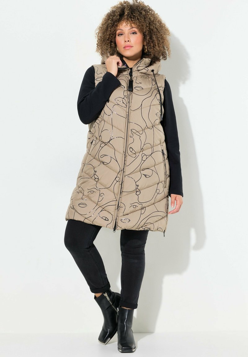 Beige gesteppte Weste mit abstrakten Gesichts-Linienmustern, einem Reißverschluss vorne und Kapuze, kombiniert mit schwarzen Slim-Fit-Hosen und Ankle-Boots.