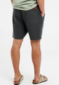 Shorts pour hommes gris foncé avec un motif texturé, dotés d'une poche arrière et d'un petit écusson en cuir brun sur la ceinture.