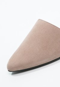 Avant d’une chaussure en daim beige à bout pointu avec des coutures nettes et une fine semelle noire sur fond blanc.