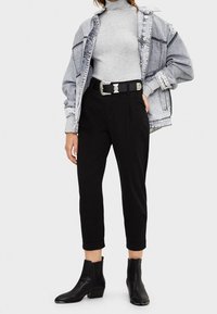 Col roulé côtelé gris, veste en denim oversize usée, pantalons noirs fuselés et bottines noires à talon bloc.