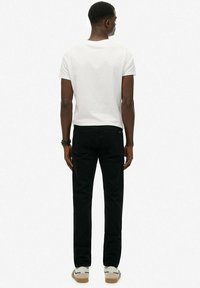 Jeans negros con un diseño de pierna recta, combinados con una camiseta blanca básica. Presentan un estilo minimalista y un sutil detalle en el bolsillo trasero.