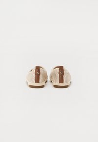Et par beige vevd slip-on sko med brune lærtrekk ved baksiden mot en hvit bakgrunn.