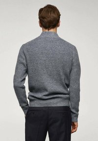 Pull gris en maille avec un col haut, une texture côtelée et des manches longues. La vue de dos montre une coupe ajustée et des coutures cintrées.