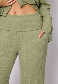 Ensemble de loungewear en tricot côtelé dans une teinte verte douce ; taille large, coupe ample, poches dans le pantalon, texture douce et rayures verticales.