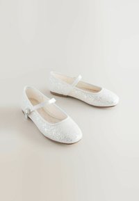 Ballerine bianche glitterate con punta tonda, cinturino alla caviglia e un piccolo bottone decorativo. Parte superiore in morbido tessuto e design con suola piatta.