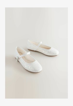 Białe błyszczące baletki z zaokrąglonym czubkiem, paskiem na kostce i małym dekoracyjnym guzikiem. Górna część z miękkiego materiału i płaska podeszwa.