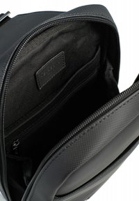 Zaino nero con superficie texturizzata, chiusura con zip e tasca interna con fodera liscia e etichetta di marca.