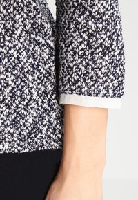 Stickad tröja med marinblå och vit spettermönster. Har trekvartslånga ärmar med en kontrasterande ljus krage.