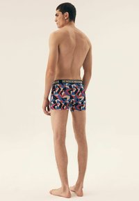 Męskie bokserki charakteryzują się geometrycznym wzorem w odcieniach niebieskiego, czerwonego i szarego. Miękka tkanina z czarnym pasem z napisem "HENDERSON".