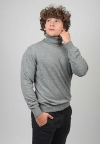 Grå turtle neck-tröja i mjukt stickat material, med långa ärmar och ribbade mudd. Modellen poserar mot en neutral bakgrund.