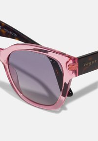 Rozā caurspīdīgas kaķa acs saulesbrilles ar polaroid stikliem. Bruņurupuča raksta sānu rokturi ar zelta zīmolu logo. Gluda apdare un izteikta forma.