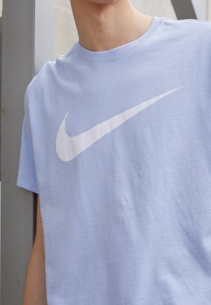 Helles blaues Baumwoll-T-Shirt mit kurzen Ärmeln und Rundhalsausschnitt. Auf der Vorderseite befindet sich ein großes weißes Nike-Logo. Glatte Textur.