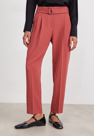 Pantalon rouge taille haute avec ceinture et plis, porté avec un haut noir à manches longues et des ballerines Mary Jane en cuir verni noir.