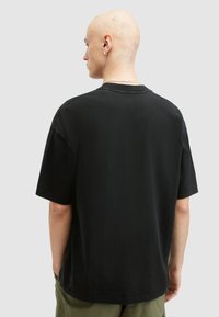 Svart bomulls-T-shirt med avslappnad passform, rundad halsringning och korta ärmar, sedd bakifrån, i kombination med olivgröna byxor.