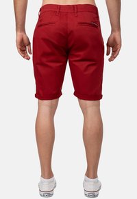 Rode katoen shorts met opgerolde mouwen, voorzien van twee achterzakken en subtiele stikseldetails, gecombineerd met witte sneakers.