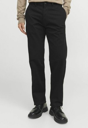 Pantaloni neri in misto cotone con design a gamba dritta, tasche frontali e chiusura a bottone. Abbinati a scarpe in pelle nera.
