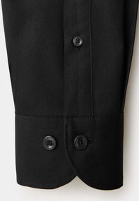 Manche de chemise noire avec poignets à double bouton et patte de boutonnage verticale sur un tissu texturé.