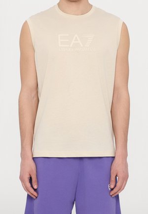 Camisa sin mangas beige con logo en relieve EA7 Emporio Armani, usada con pantalones cortos morados, mostrada desde el cuello hasta las caderas.