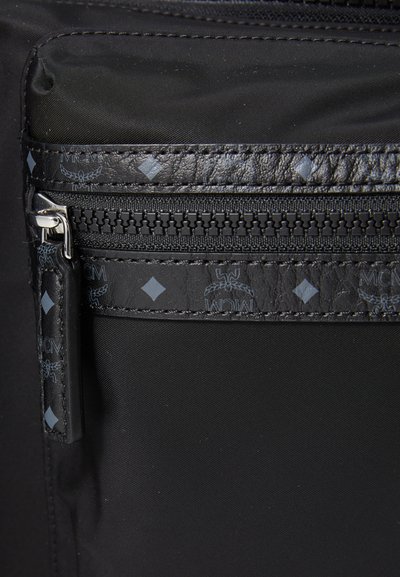 Black fabric bag detail featuring a zippered pocket with a textured black leather trim and subtle diamond pattern accents.