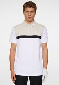 Herrarnas polotröja i vitt, med ljusgrå axlar och ett svart horisontellt rand över bröstet, med en tre-knappsknäppning.