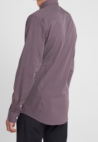 Camicia a maniche lunghe da uomo color marrone bordeaux con un motivo geometrico. Presenta un colletto aperto e polsini con bottoni, realizzata in un tessuto morbido.