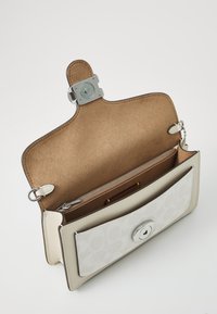 Läderhandväska med en ljusbeige utsida, vit mönstrad klaff och en slät inredning. Har ett silverfärgat lås och en dragkedjeficka.