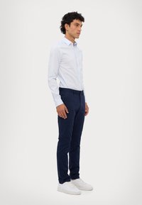 Lyseblå skjorte med knapper, marineblå bukser og hvite sneakers. Skjorten har krage og knapper; buksene sitter godt med en glatt tekstur.