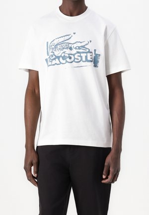 Weißes Baumwoll-T-Shirt mit einem blauen grafischen Logo-Design eines Krokodils mit Text. Kurze Ärmel und lockere Passform.