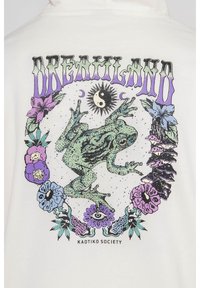 Bílá mikina s kapucí, která obsahuje centrální grafiku zelené žáby obklopené barevnými květinami, měsícem, sluncem a textem "DREAMLAND" v purpurové barvě.