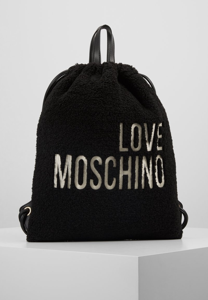 Svart fleece-ryggsäck med snörstängning, prydd med "LOVE MOSCHINO" i metallisk text. Inkluderar svarta läderremmar och guldfärgade detaljer.