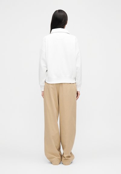 Sudadera blanca de gran tamaño con ribete acanalado en el dobladillo y el cuello, combinada con pantalones de pierna ancha color beige claro, que muestran un ajuste relajado y una textura suave.