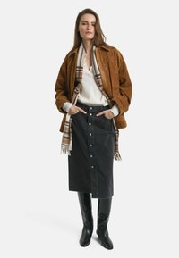 Giubbotto di suede marrone, maglione crema, gonna in denim nera con bottoni e stivali alti in pelle nera, completati da una sciarpa a quadri.
